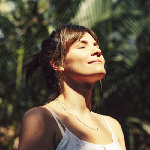 Beautiful Happy Woman Enjoying the Warm Sunlight in a Tropical Public Park Close up upper body shot of a beautiful happy young Caucasian woman enjoying the warm sunlight and tropical atmosphere with her eyes closed surrounded by palm trees in a tropical public park.