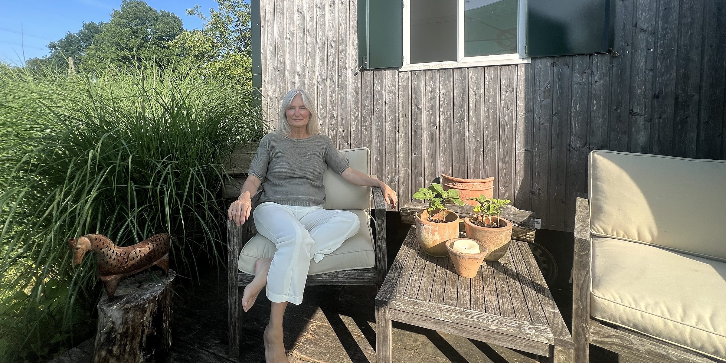 Angelika Allroggen sitzt entspannt in einem Gartensessel vor einer Holzhütte, daneben ein freier Sessel