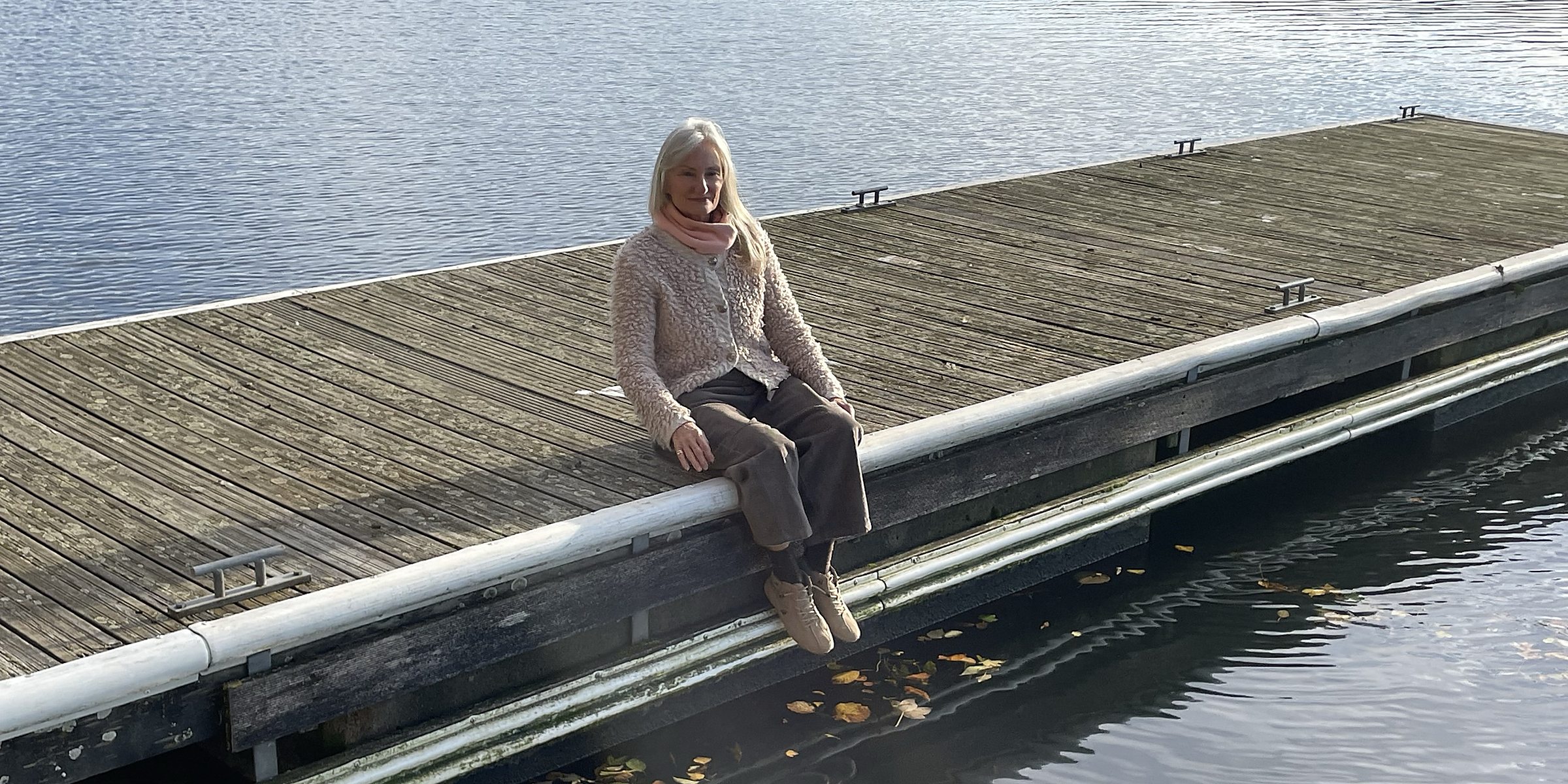Angelika Allroggen sitzt still auf einem Bootssteg am See und blickt nach unten