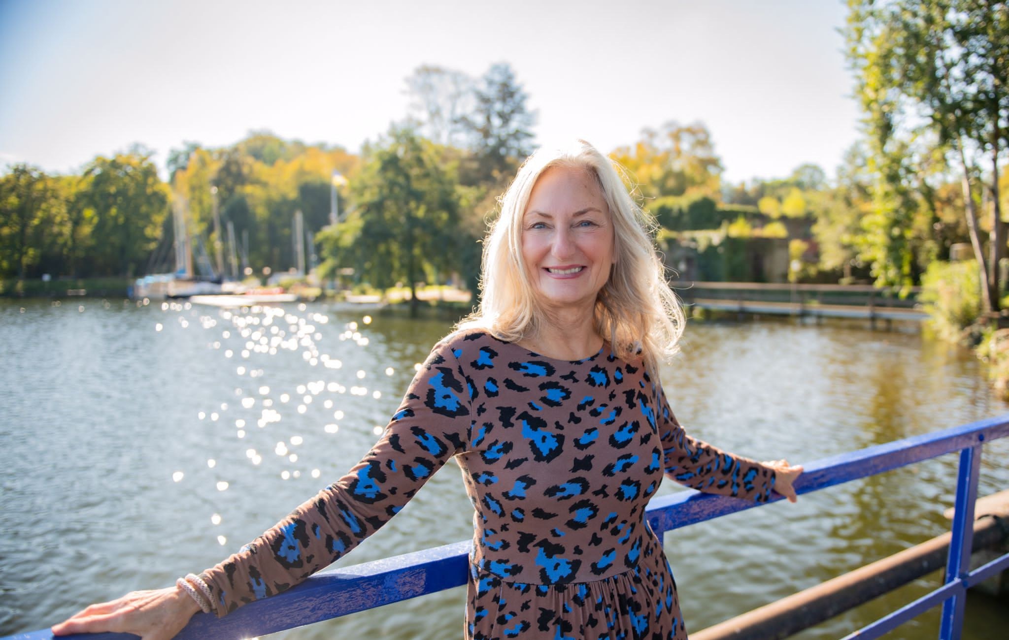 Mein Wirken - Portraet am Wasser Angelika Allroggen lächelnd am Geländer vor einem sonnigen See